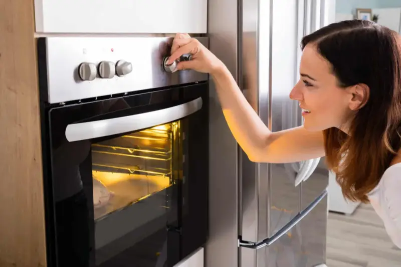 Une femme ajuste le bouton du four pour savoir à quelle température faire réchauffer un plat. Le plat est visible à travers la vitre.